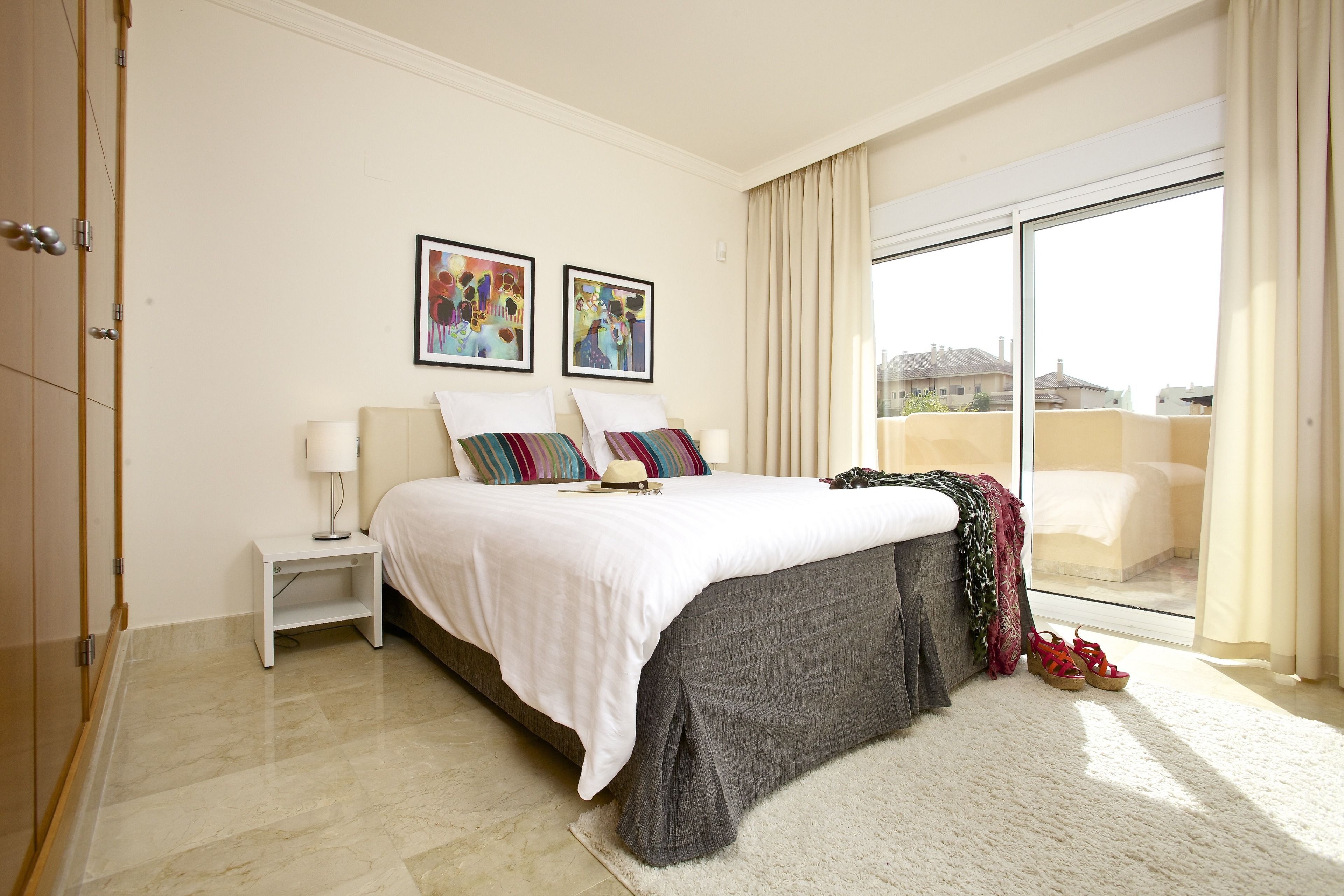 Un dormitorio con cama, mesita de noche, ventana con cortinas y vista al exterior.