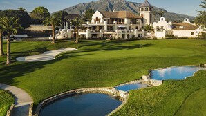 Un campo da golf con un club house, palme e una montagna sullo sfondo.