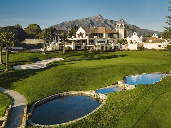 A golf course with a clubhouse, palm trees, and a mountain in the background.