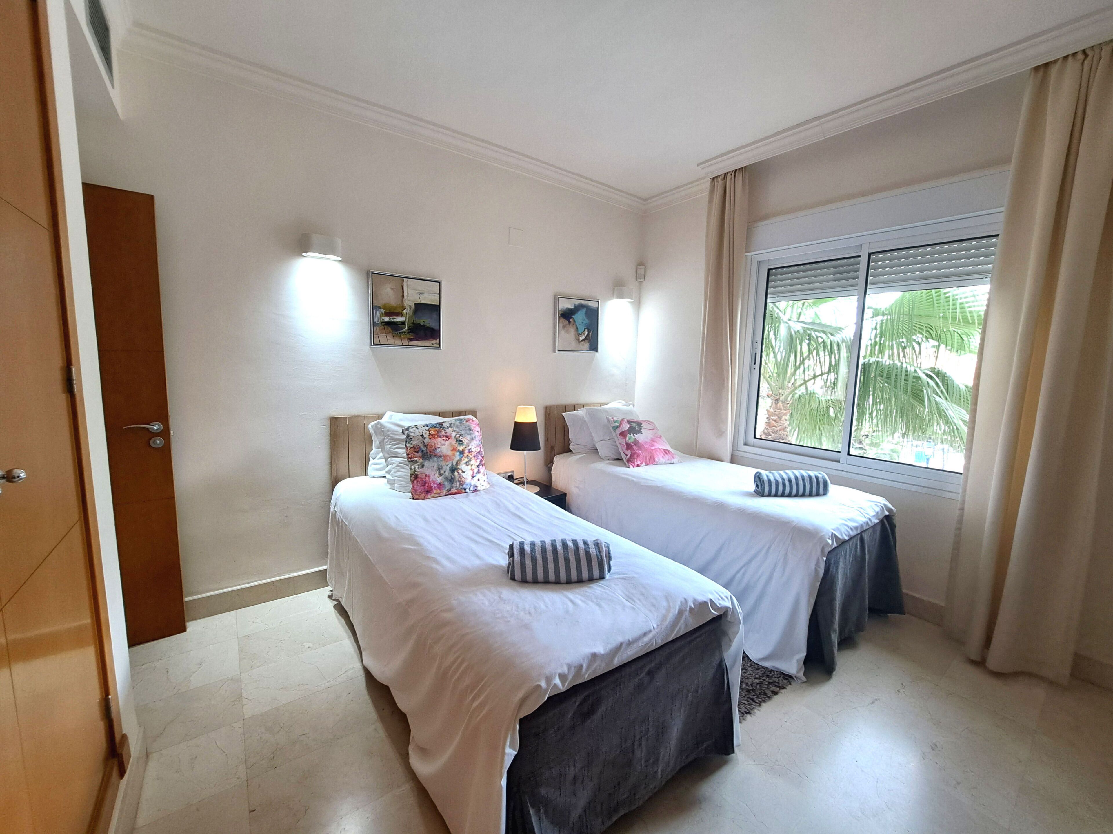 Een hotelkamer met twee bedden, een raam met gordijnen, een deur en een muur met twee foto's.