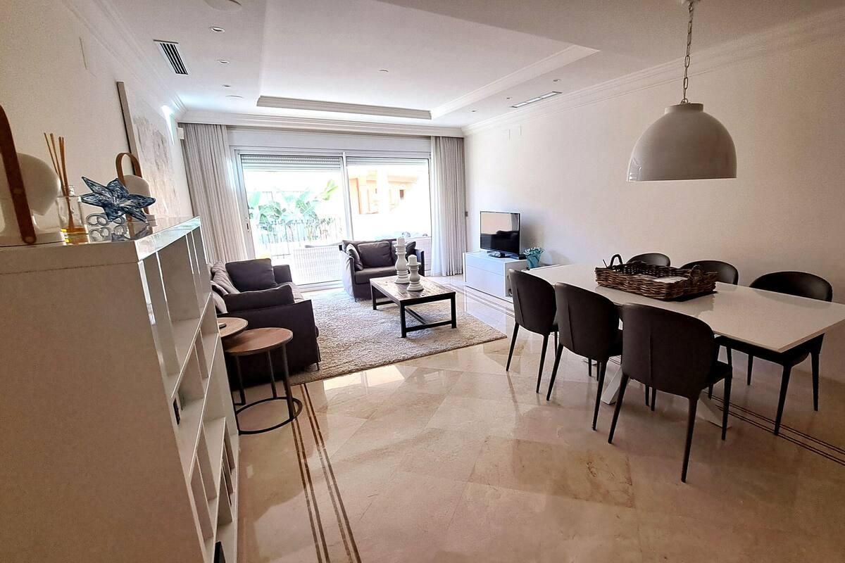 A modern living room with a dining area, a TV, and a large window with curtains.