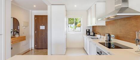 A modern kitchen with white cabinetry, a stainless steel range hood, and a window with a view of greenery.