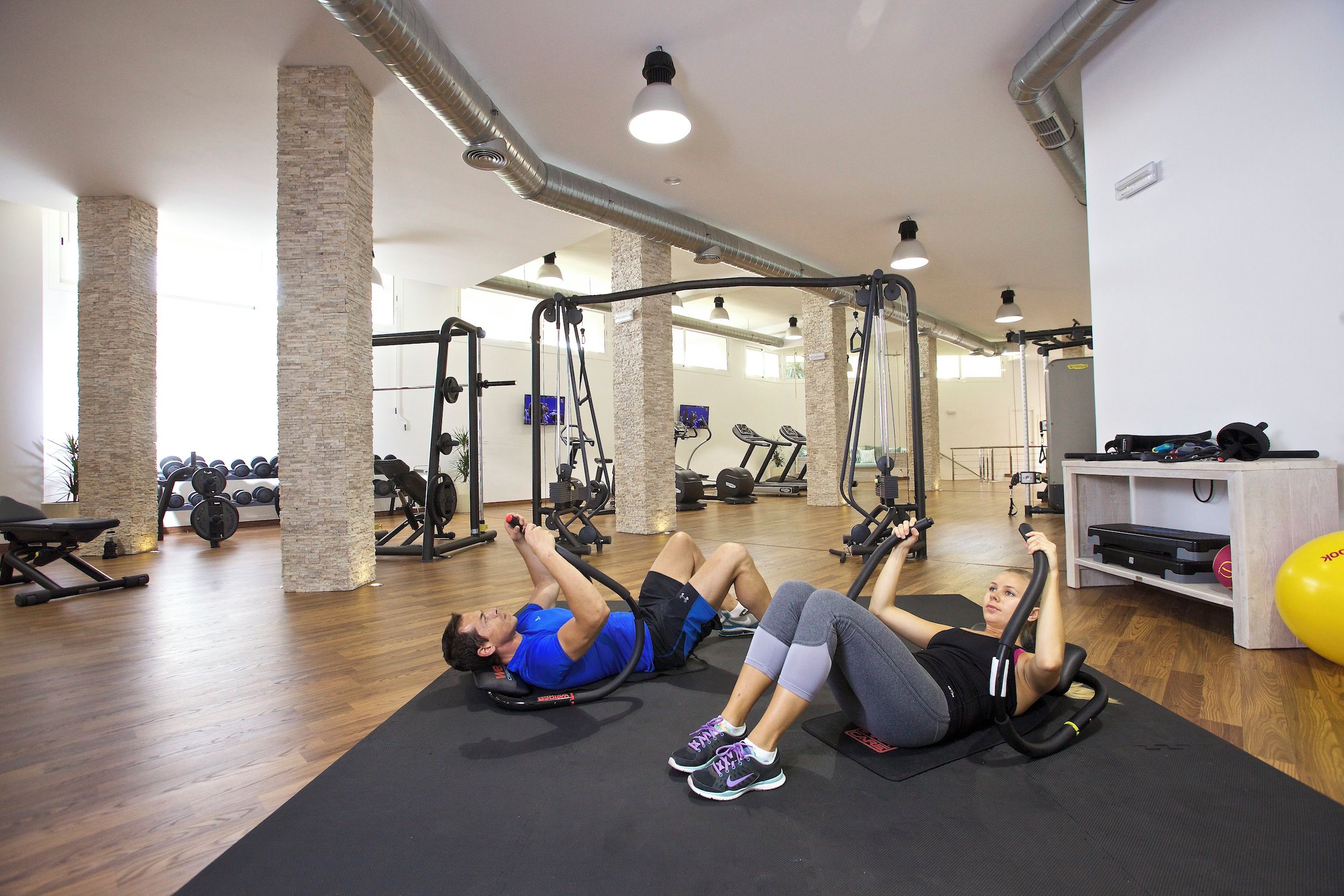 A gym with exercise equipment, wooden floors, and brick pillars.