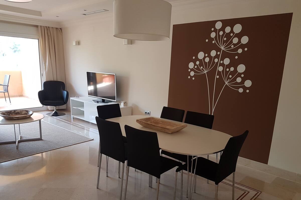A modern dining area with a round table, black chairs, a television, and a decorative wall panel.