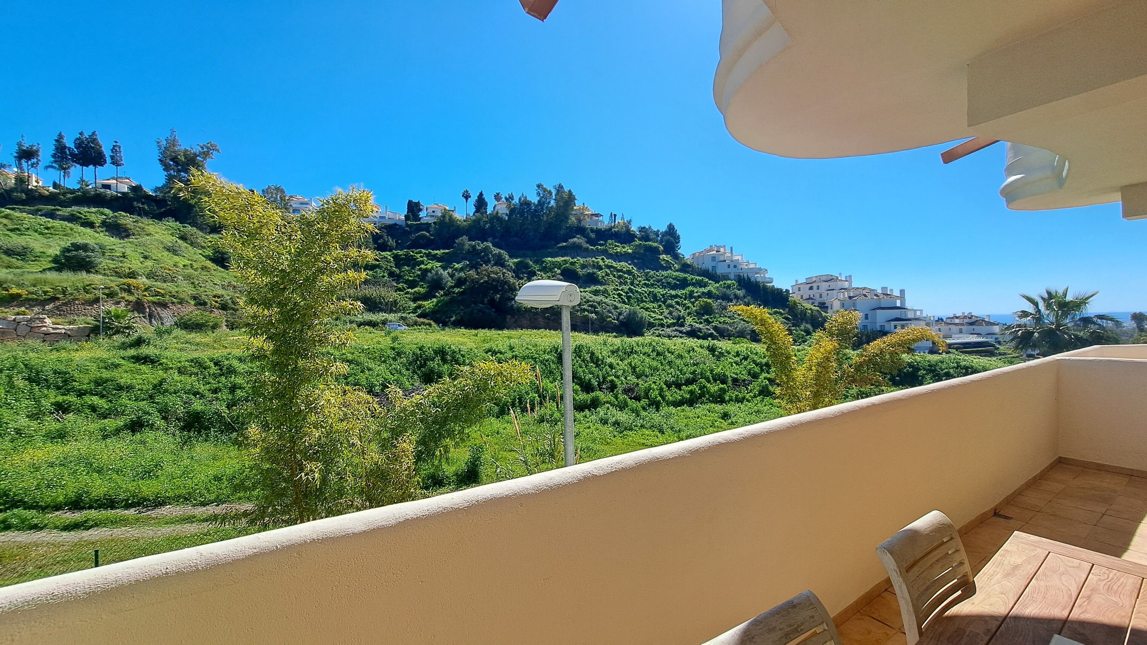 A balcony with a view of a green hillside, a street lamp, and a clear blue sky.