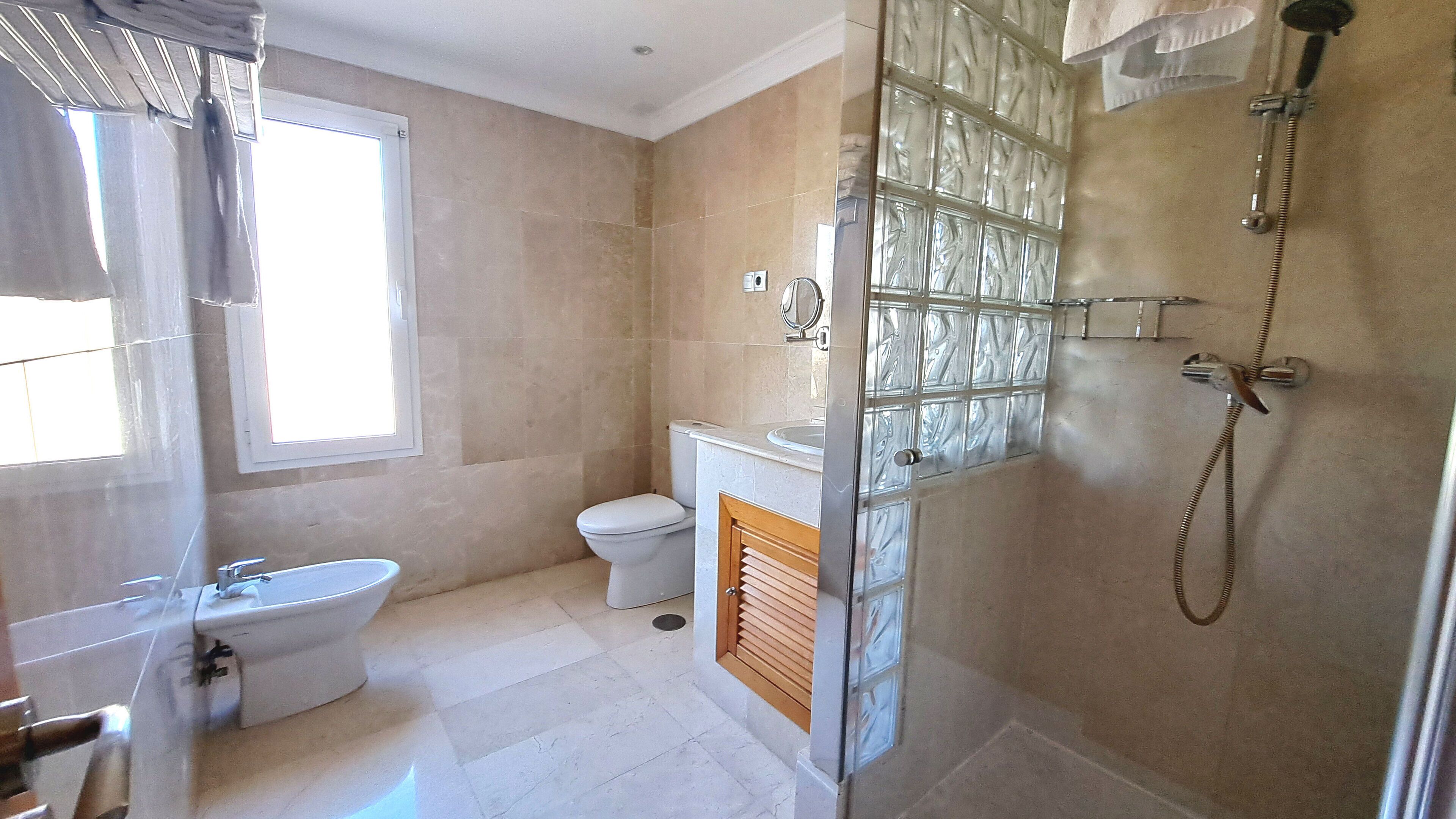 Un baño con inodoro, bidé y zona de ducha con mampara de vidrio.