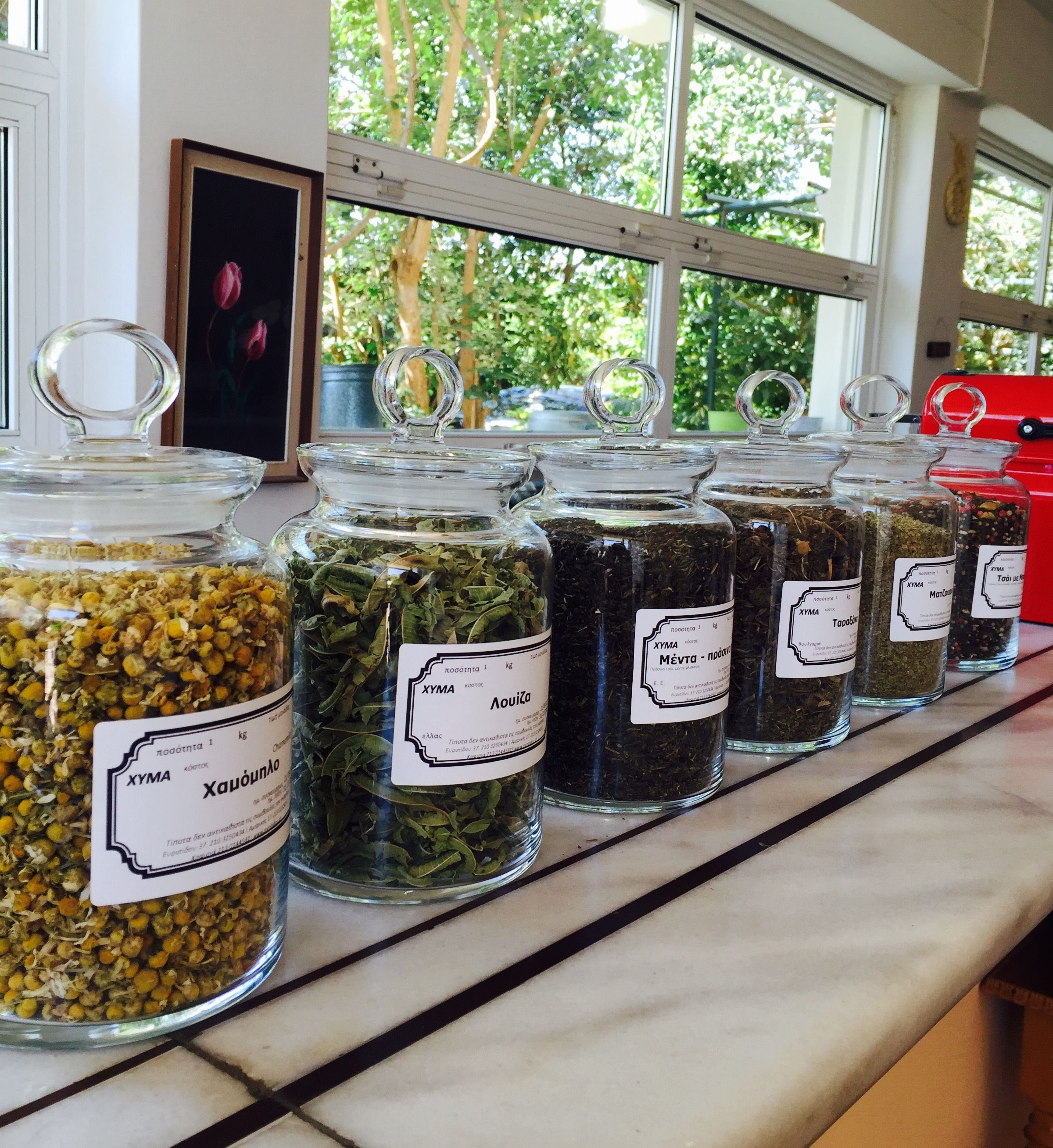 A row of glass jars with labels on a shelf, each containing different herbs and spices.
