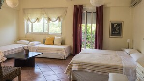 Une chambre d’hôtel avec deux lits, une petite table et une chaise. Il y a une fenêtre avec des rideaux et une vue sur la verdure à l’extérieur.
