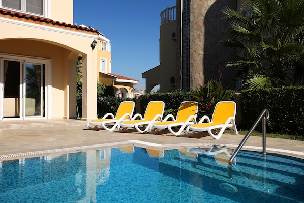 A swimming pool with yellow lounge chairs and a clear blue sky.