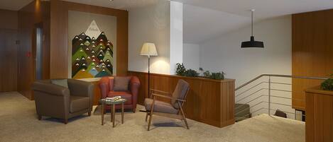 A lobby with a reception desk, two sofas, a table, a lamp, and a staircase.