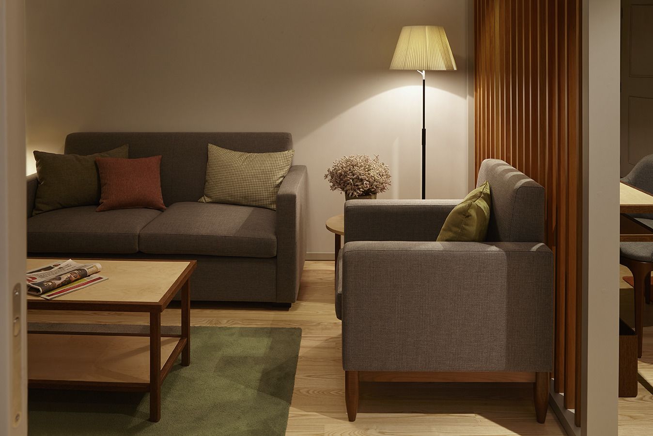 A living room with a sofa, armchair, coffee table, and a floor lamp.