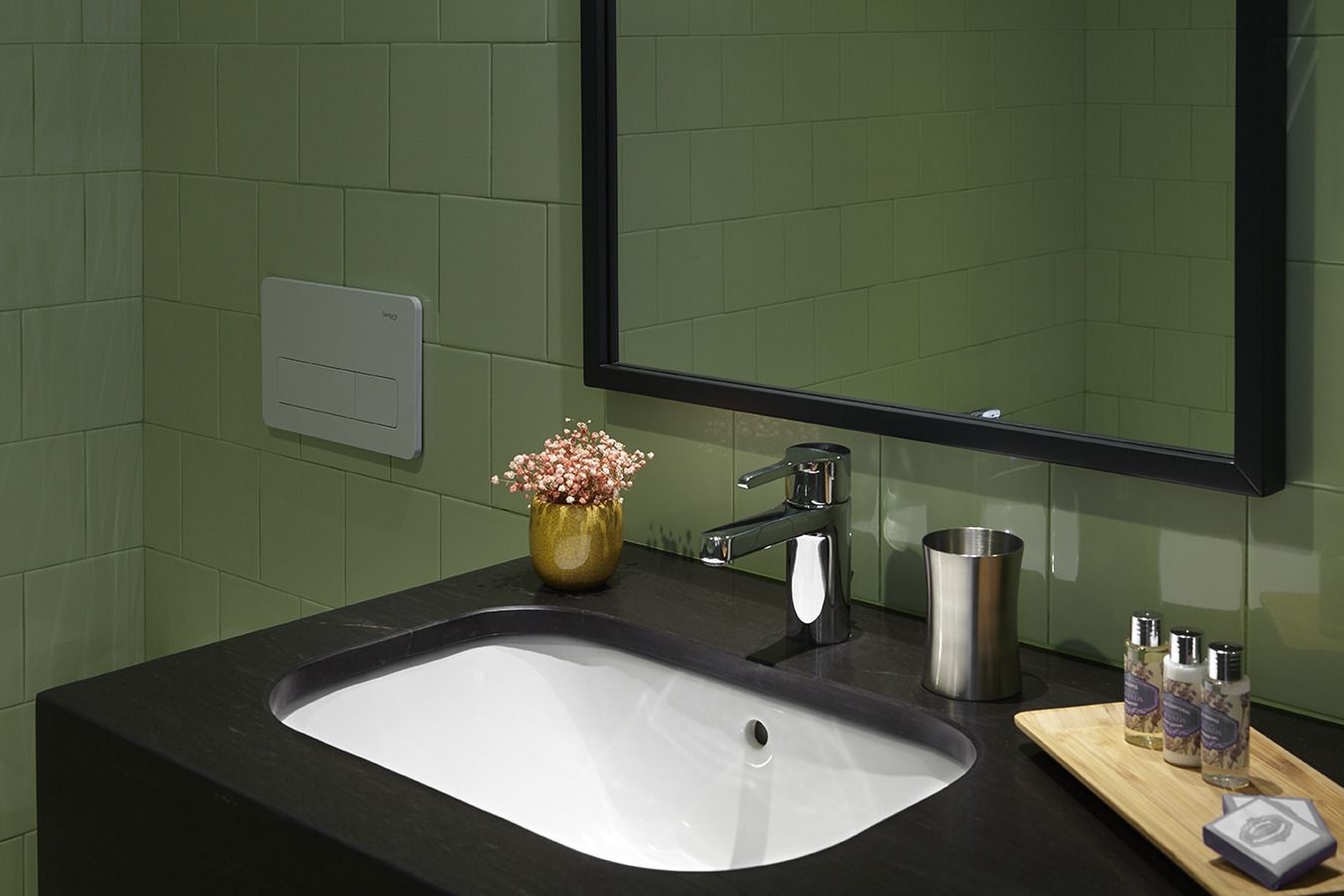 A bathroom with a black countertop, a white sink, a gold vase with flowers, a stainless steel faucet, and a mirror.
