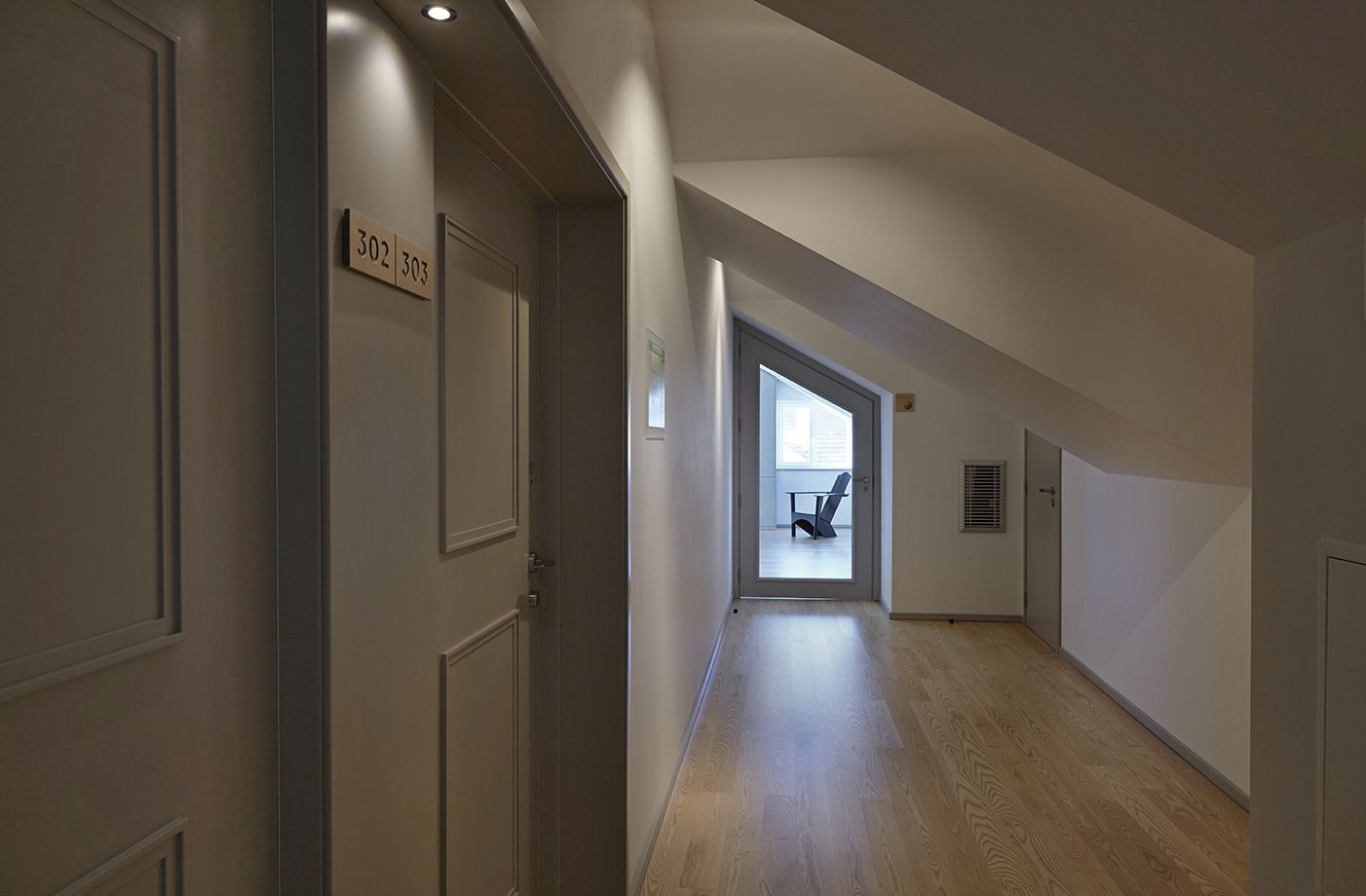 A hallway with doors labeled 302 and 303, leading to a room with a chair and a window.