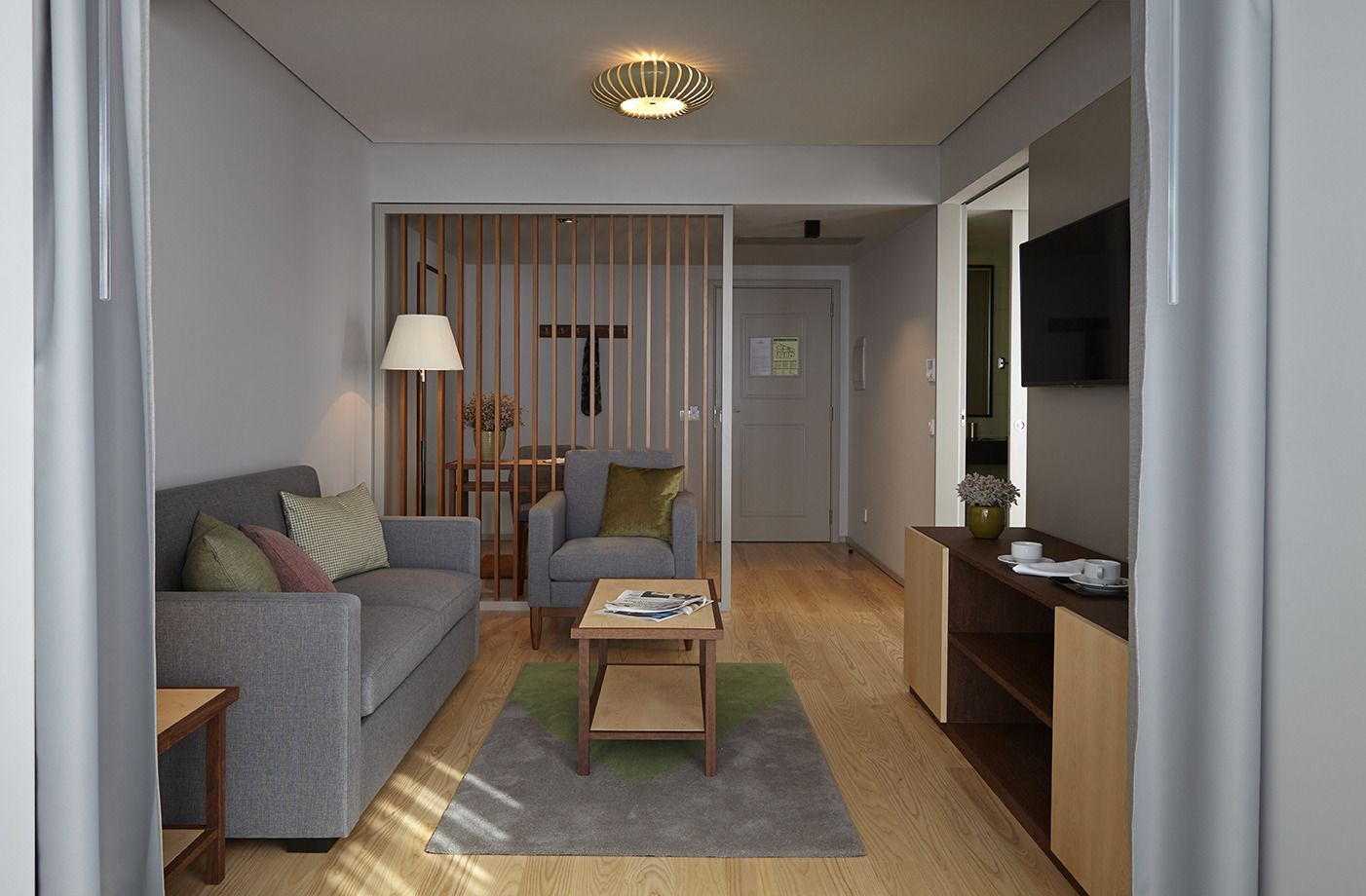 Una sala de estar moderna con un sofá gris, dos sillones, una mesa de centro y un televisor sobre un mueble de madera.