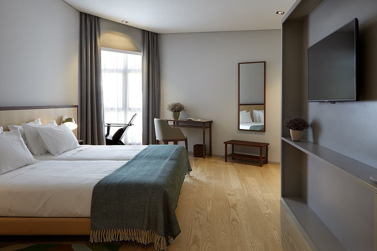 A hotel room with a bed, a desk, a chair, a TV, and a mirror.