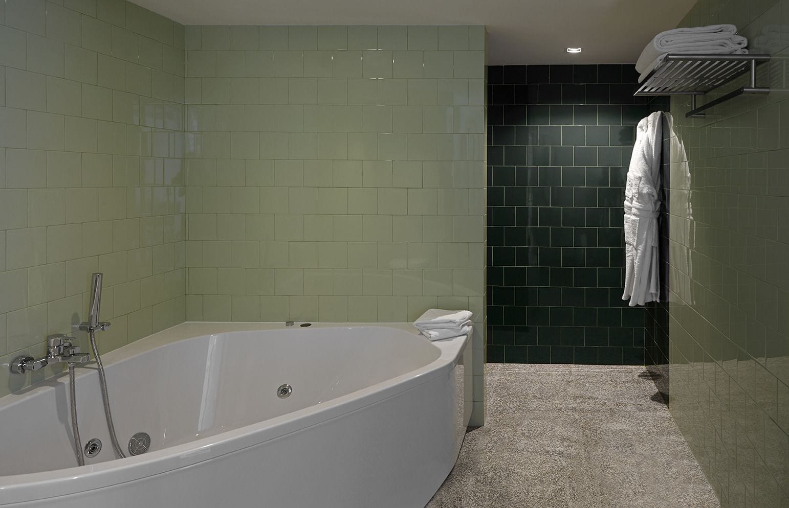 Une salle de bain moderne avec une baignoire sur pieds, des murs recouverts de carreaux verts et noirs, et un porte-serviettes avec des serviettes pliées.