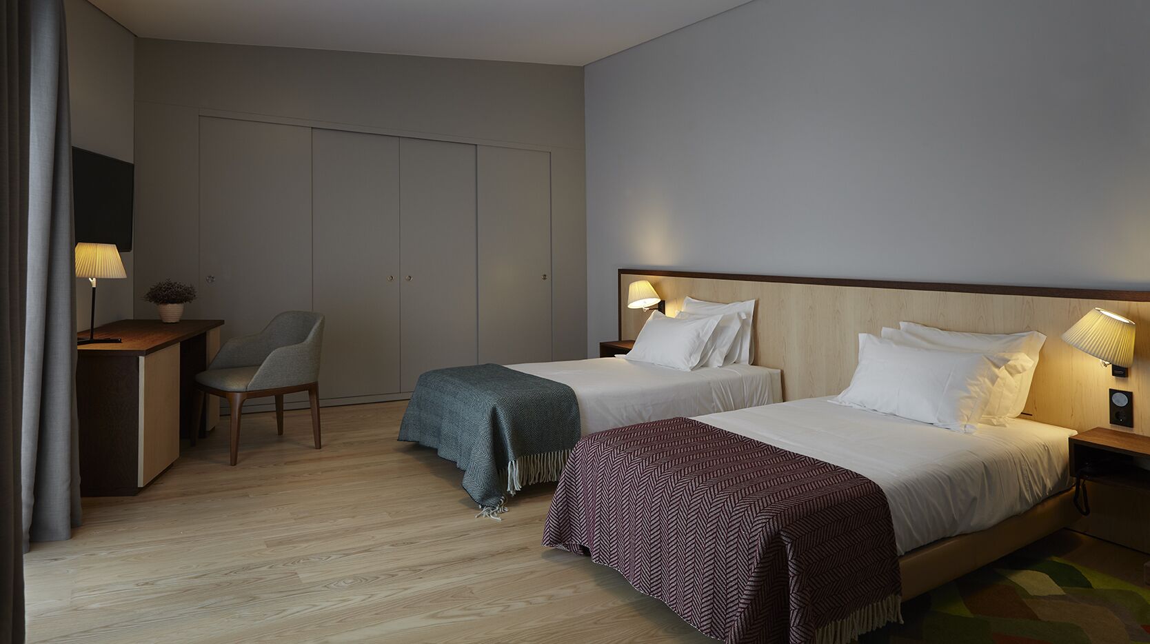 Habitación de hotel con dos camas, un escritorio, una silla y una lámpara.