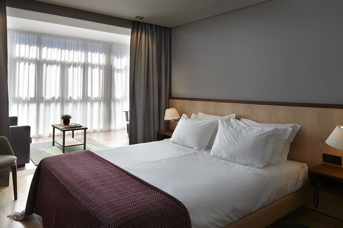 A hotel room with a large bed, a chair, a small table, and a lamp.