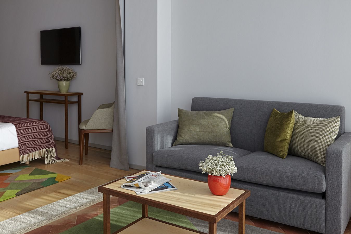 Een moderne woonkamer met een grijze bank, een houten salontafel, een klein bijzettafeltje, een stoel en een flatscreen televisie aan de muur.