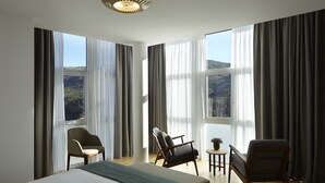 Une chambre d’hôtel avec un grand lit, deux fauteuils, une petite table et une vue sur l’extérieur.