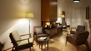 Un salon chaleureux avec une cheminée, des fauteuils confortables et une lampe moderne.