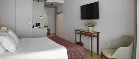 A hotel room with a bed, a chair, a table, a TV, and a small plant.