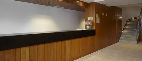 A reception area with a wooden reception desk, a potted plant, and a staircase leading to an upper floor.