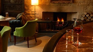 Una habitación acogedora con chimenea, un sillón verde, una mesa con vasos y un cuadro en la pared.