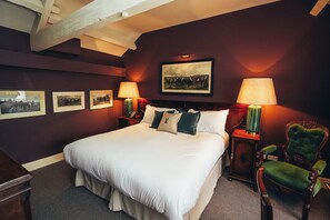 A large bed with white linens, two bedside tables with lamps, a green upholstered chair, and framed pictures on the wall. - The Peacock at Rowsley (Matlock)