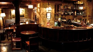 Un rincón acogedor de bar con mobiliario de madera, paredes de piedra y una variedad de botellas en estantes.