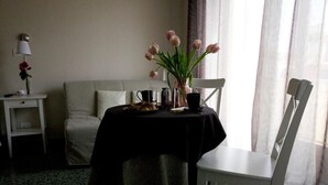 A hotel room with a bed, a small table with a black tablecloth, a vase with pink flowers, a chair, a lamp, and a window with curtains. - La Casa In Prati (Rome)