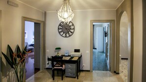 A hallway with a desk, chair, and a clock on the wall. There is a plant on the left and a door on the right. - La Casa In Prati (Rome)