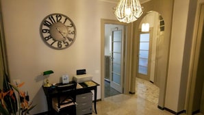 A hallway with a wall clock, a desk with a lamp, and a door leading to another room. - La Casa In Prati (Rome)