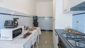 A compact kitchen with a microwave, stove, and a small dining table set for two. - La Casa In Prati (Rome)
