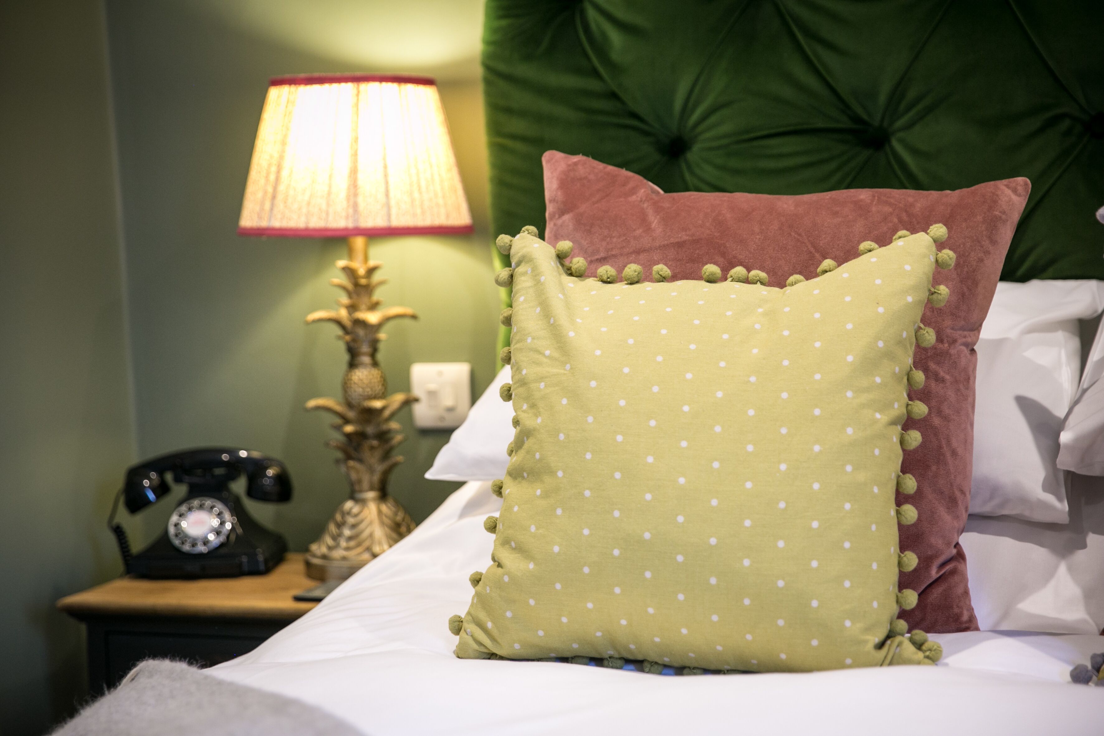 Un lit avec un oreiller à pois verts et un oreiller marron, une lampe et un téléphone à cadran sur une table de chevet.