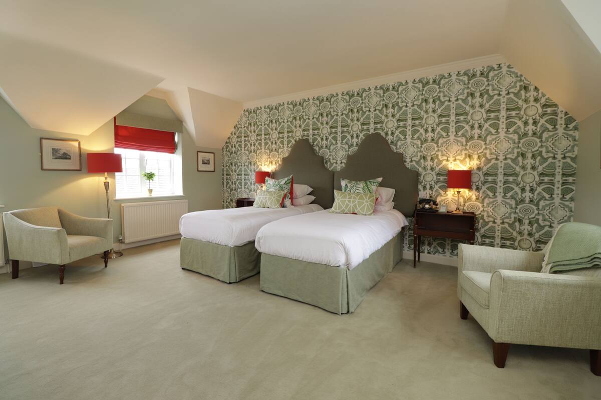 A bedroom with two beds, a chair, a lamp, and a patterned wall.