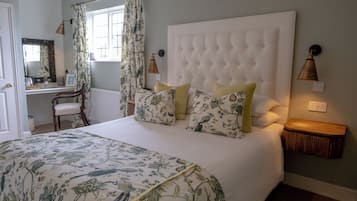 A bedroom with a large bed, floral bedding, a wooden nightstand, and a desk with a chair.