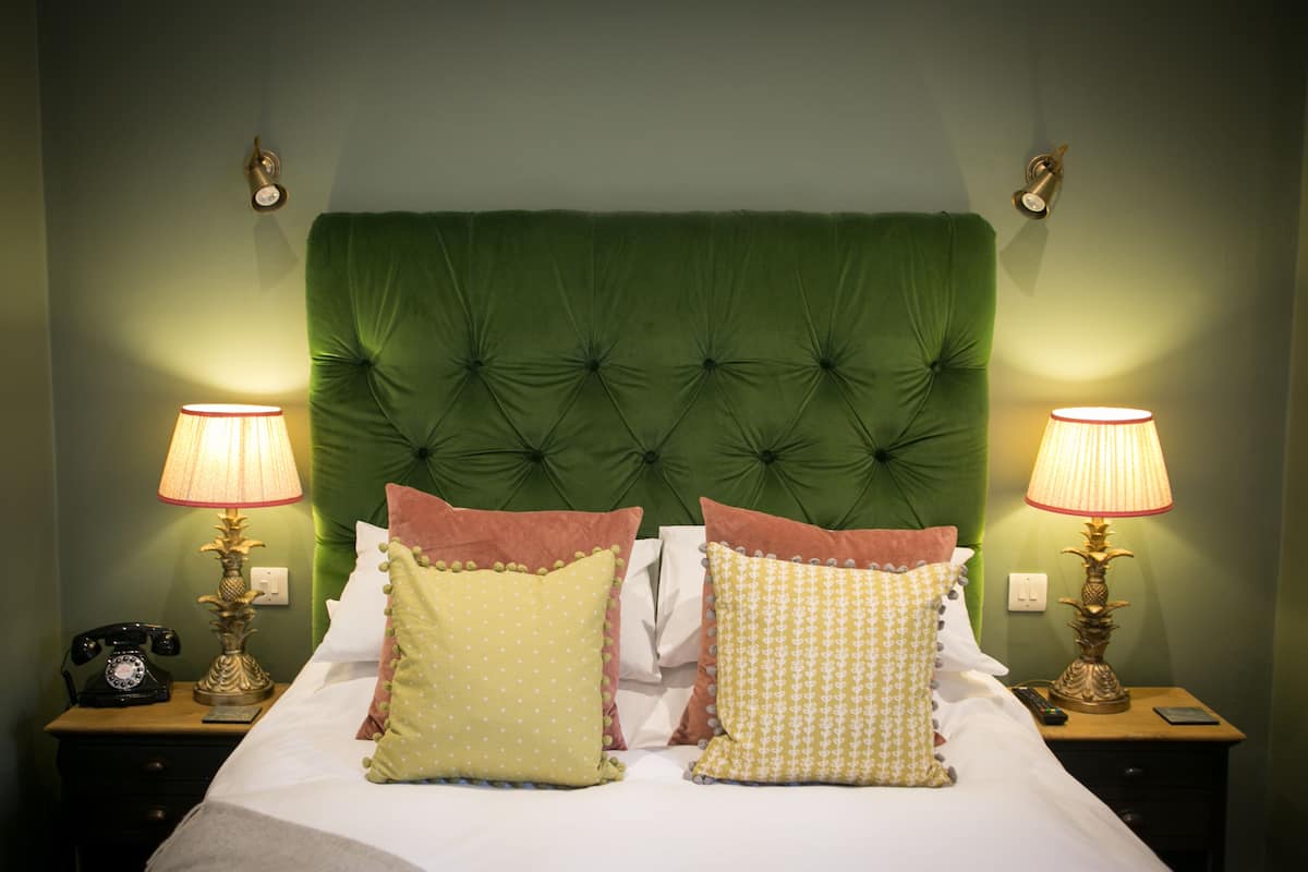 A neatly made bed with a green upholstered headboard, two bedside lamps, and a telephone on a wooden nightstand.