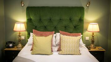A neatly made bed with a green upholstered headboard, two bedside lamps, and a telephone on a wooden nightstand.