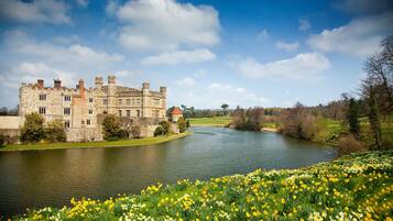 A historic stone building with a river in front, surrounded by lush greenery and daffodils.