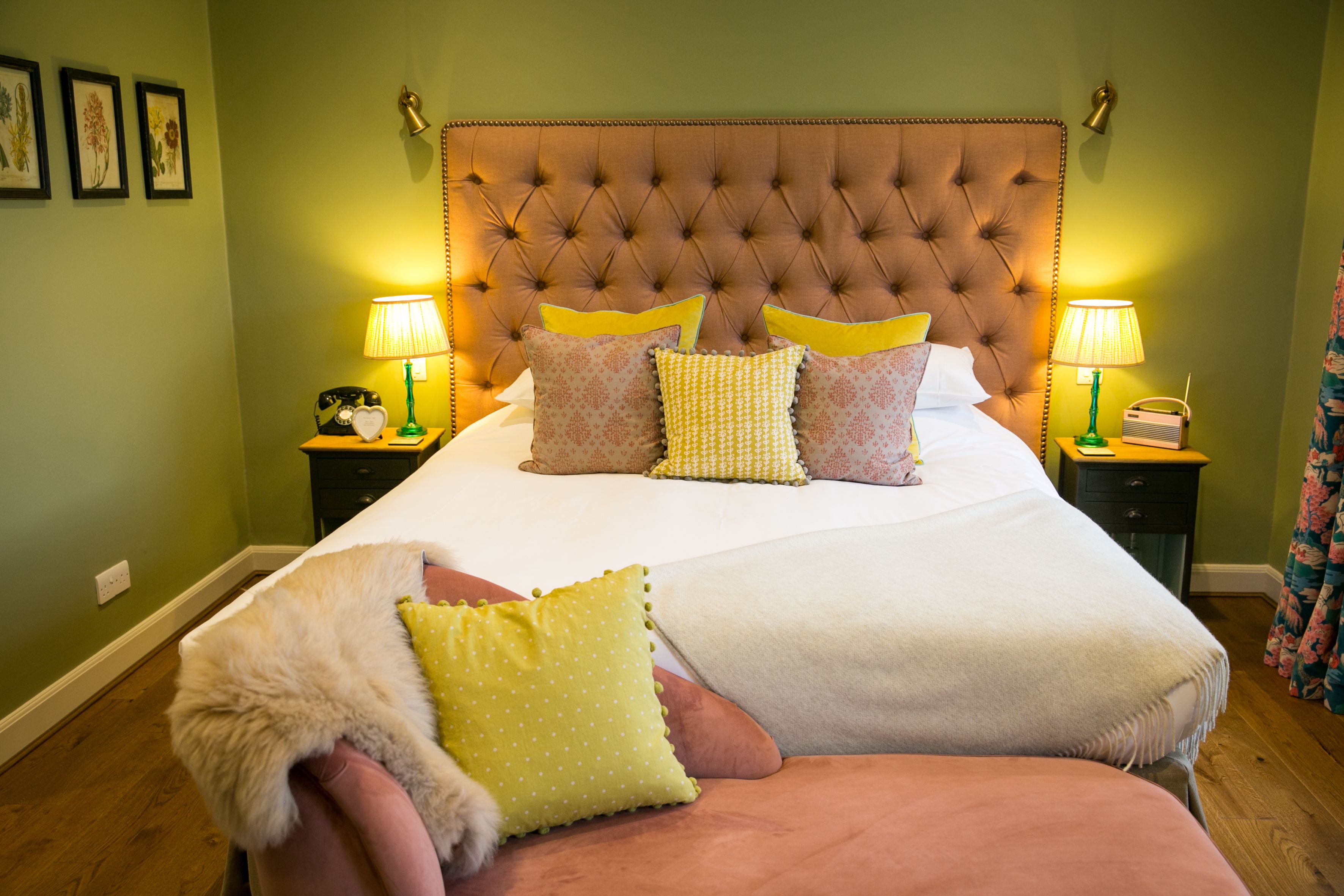 A neatly made bed with a tufted headboard, two bedside tables with lamps, and a fluffy chair with a throw blanket.
