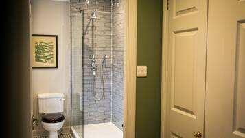 A bathroom with a toilet, a shower with a glass door, and a door with a brass handle.