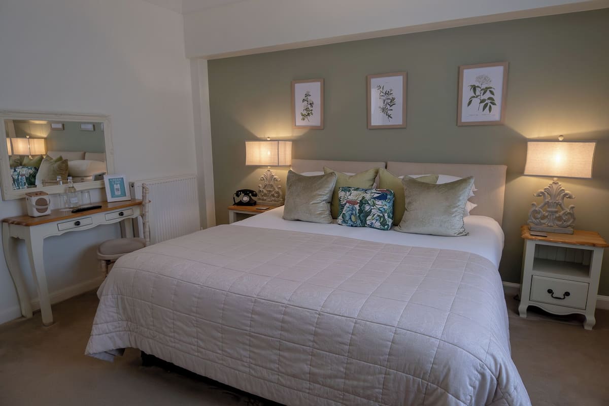 A bedroom with a large bed, bedside tables, a dresser, a mirror, and wall-mounted lamps.