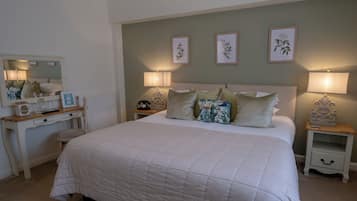 Quarto com cama grande, mesas de cabeceira, cômoda, espelho e luminárias na parede.