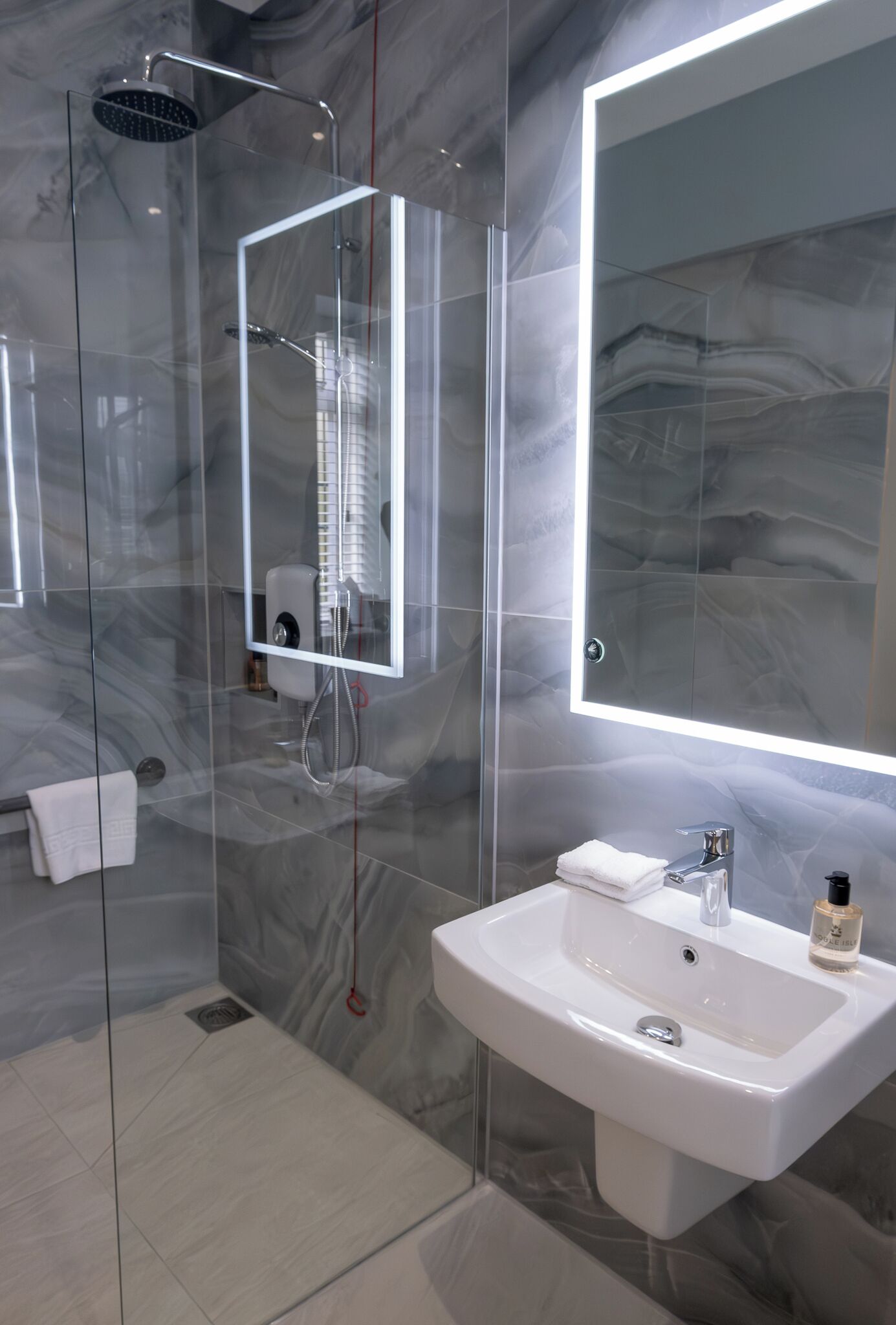 Un baño moderno con ducha de vidrio, un espejo grande y un lavabo blanco.