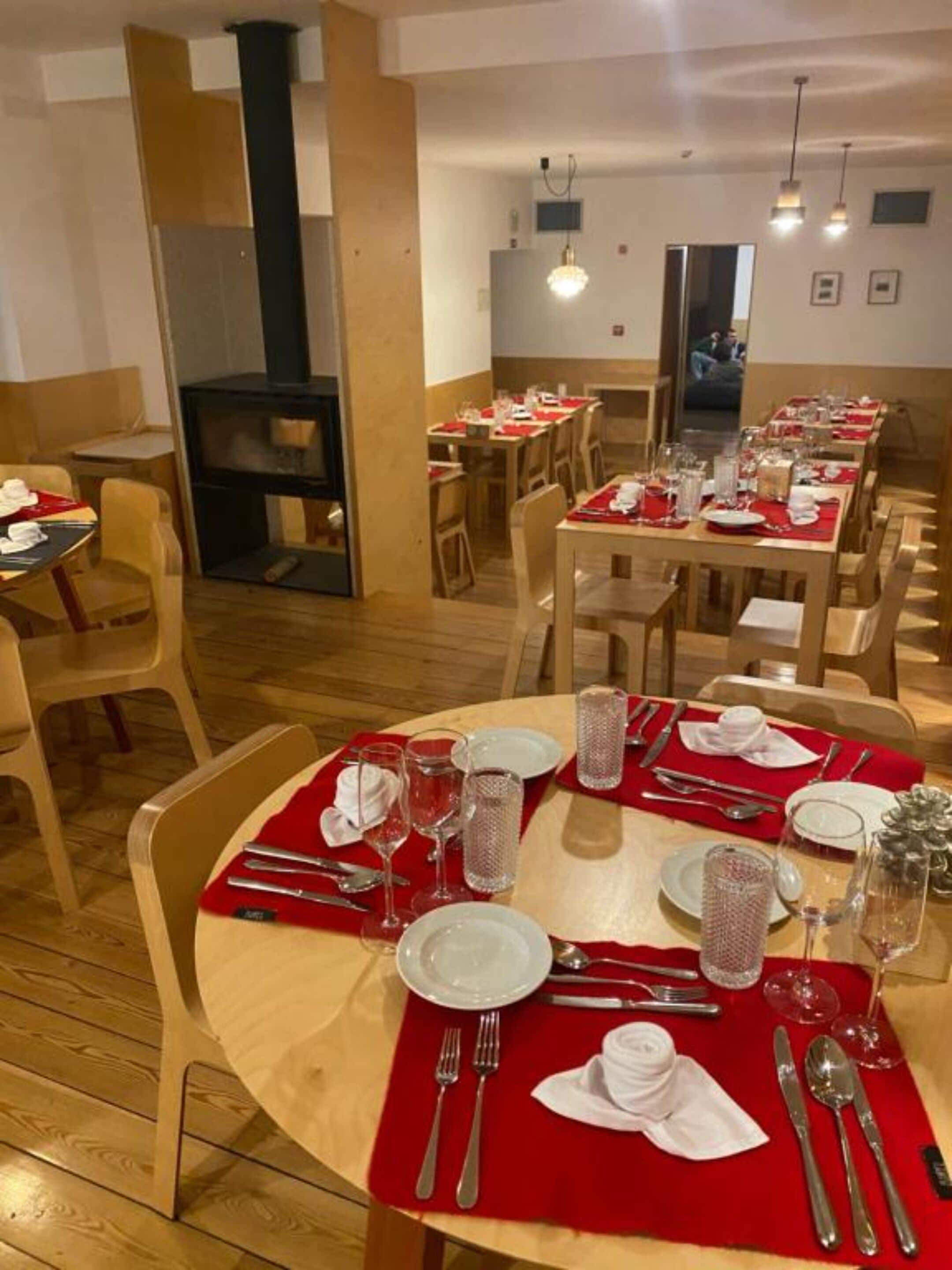 Un restaurante con mesas redondas preparadas para comer, con manteles individuales rojos y sábanas blancas.
