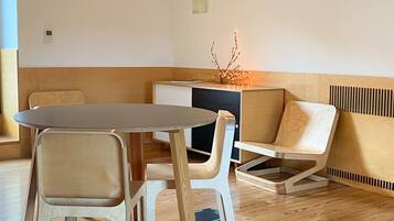 Een moderne, minimalistische kamer met houten vloer, een ronde tafel, twee stoelen, een bank en hanglampen.