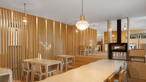 A modern dining area with wooden tables and chairs, a central chandelier, and a wooden slat wall.