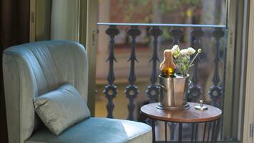Una habitación con un sillón azul, una mesita redonda con un jarrón de flores y vistas a un balcón con barandilla de metal.