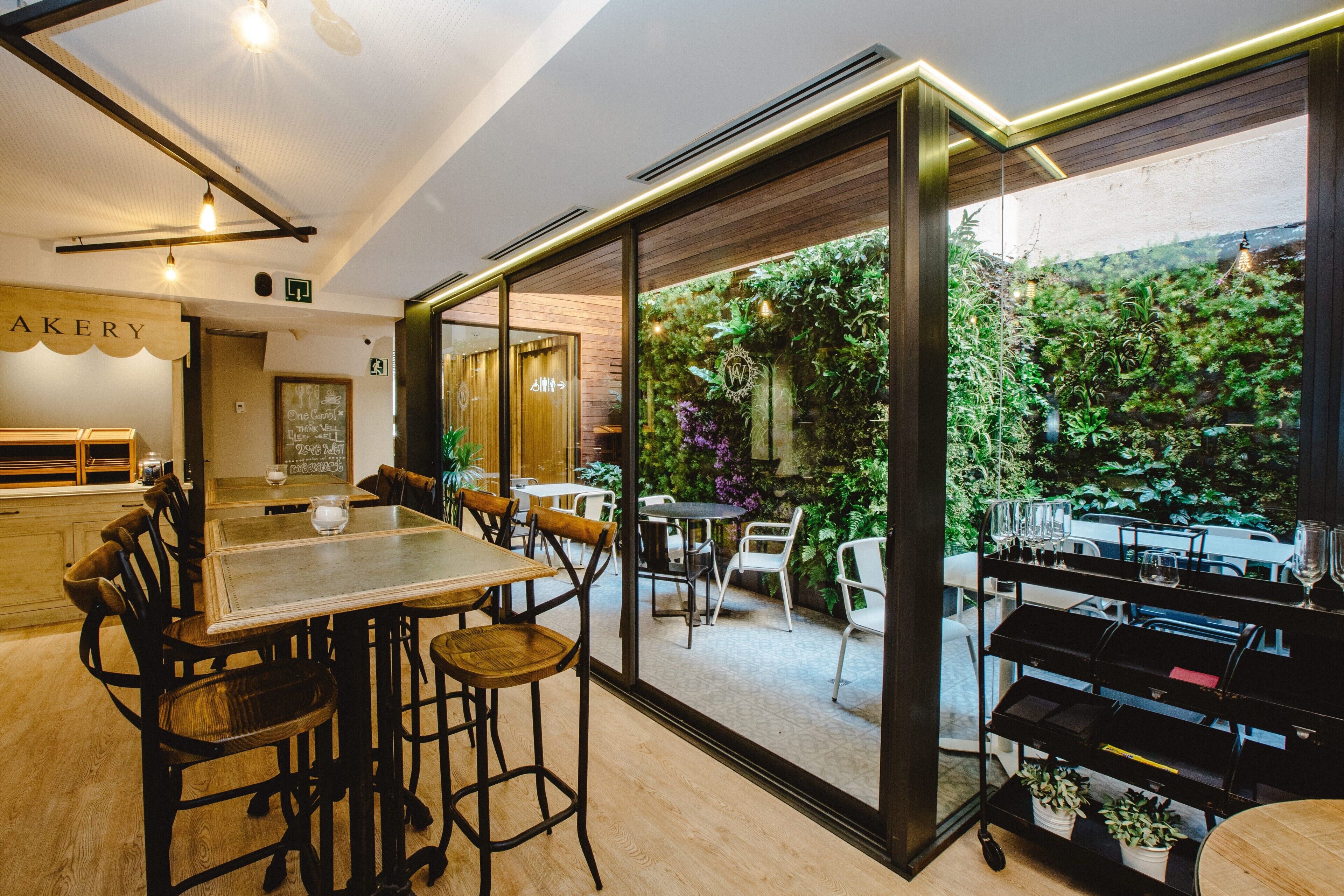 A restaurant with a bar area, seating, and a view of a lush garden.
